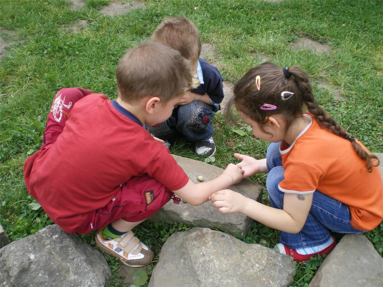 Drei Kinder hocken gebückt im Garten und schauen auf den Boden